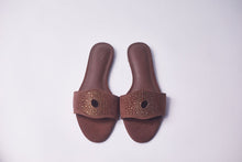 Load image into Gallery viewer, A pair of brown slide sandals with a wide strap featuring a circular cutout and a border of small metallic studs, shown on a light gray background.