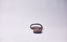 Load image into Gallery viewer, A single brown leather flat sandal shown from the back on a clean, light gray studio background.